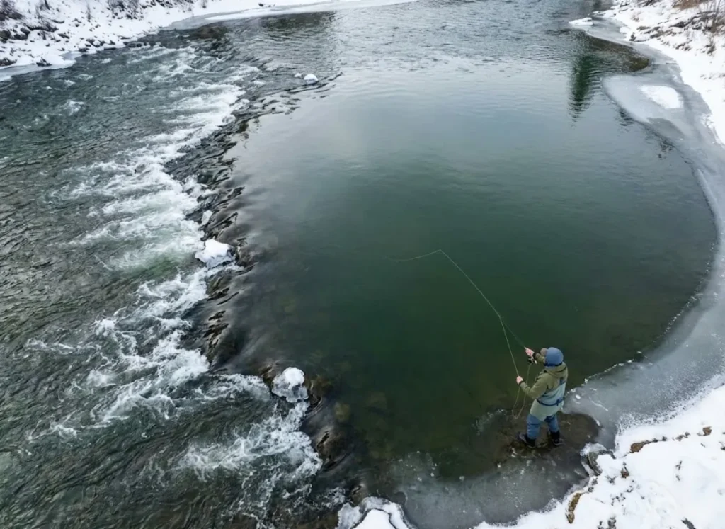 A deep, slow-moving river pool bordered by ice and snow, showing the transition from fast current to still water.