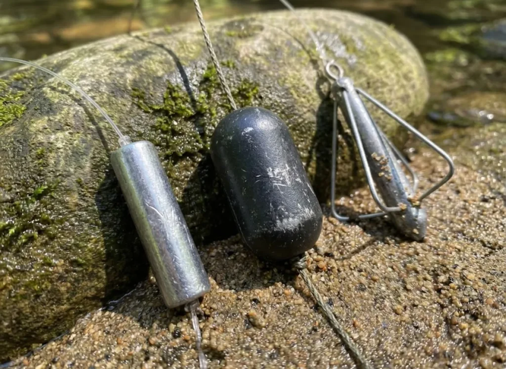 Three different types of fishing weights rigged on lines resting on a rock.