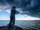 Fishing Barometric Pressure: Science & Lure Strategy An angler casting a fishing rod on a lake with a massive storm front rolling in, symbolizing rapidly falling barometric pressure.