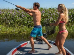 Fishing Heavy Cover: A System for Gear, Lures, and Strategy An attractive couple in their late 20s fishing for bass from a boat, casting towards thick aquatic vegetation on a sunny day.