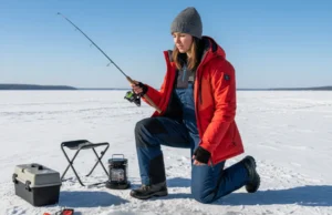 Ice Fishing Combos: Matching Gear to Your Technique A full-body shot of a young woman in modern winter gear ice fishing on a sunny day on a frozen lake.