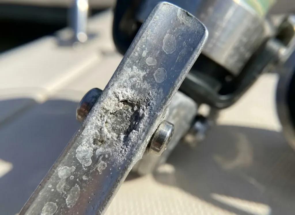 Macro shot showing white powdery corrosion and pitting on the metal frame of a saltwater fishing reel.