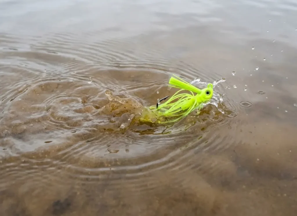 A bright fishing lure splashing into murky, stained water.