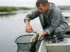 Best Fishing Tools That Won’t Rust Shut Angler using fishing pliers to unhook a bass in a rubber net, essential fishing tools on a boat gunwale