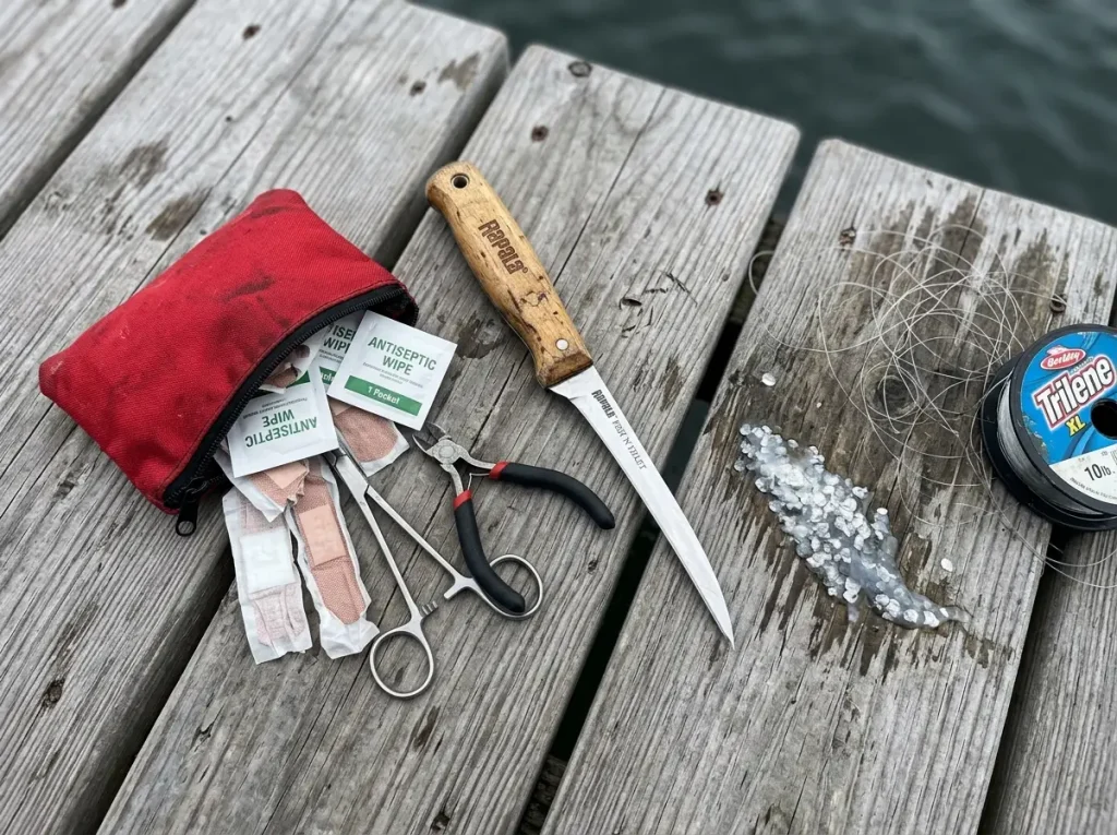 A fillet knife and a small waterproof first aid kit on a weathered dock, overlooked essential fishing tools
