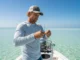 The Definitive Guide: How to Tie a Leader for Snook & Reds A skilled male angler in his late 30s tying a fishing leader on the bow of a boat in a sunny, inshore saltwater environment.