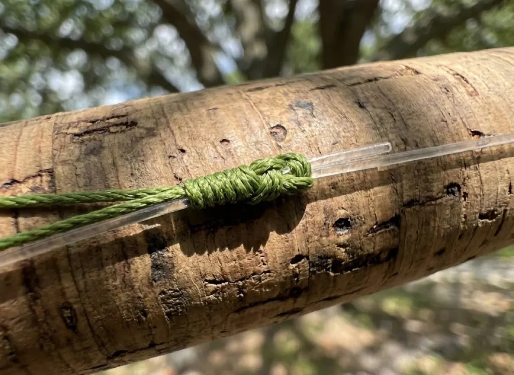 Macro view of a braided fishing line tied to a clear leader resting on a cork rod handle.