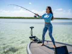 Shallow Water Anchor vs Spot Lock: A Data-Backed Analysis A beautiful female angler in athletic gear casting from a bass boat held in place by a shallow water anchor on a clear, sunny day.