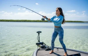 Shallow Water Anchor vs Spot Lock: A Data-Backed Analysis A beautiful female angler in athletic gear casting from a bass boat held in place by a shallow water anchor on a clear, sunny day.