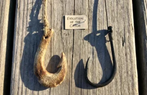 From Bone to Carbon: The Complete History of Fishing A side-by-side comparison of a prehistoric bone fish hook and a modern carbon steel hook on weathered wood.