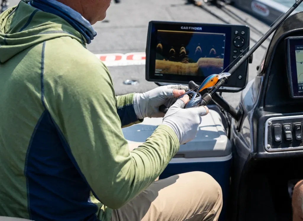 Angler analyzing a fish finder screen in bright sunlight to locate deep water bass.