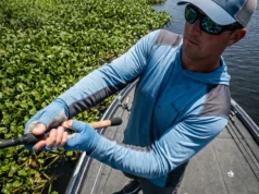 Punching for Bass: Gear, Rigs & Mat Anatomy An angler on a bass boat thrusting a heavy fishing rod downward to punch a lure through dense floating vegetation.