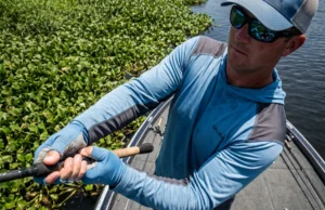 Punching for Bass: Gear, Rigs & Mat Anatomy An angler on a bass boat thrusting a heavy fishing rod downward to punch a lure through dense floating vegetation.