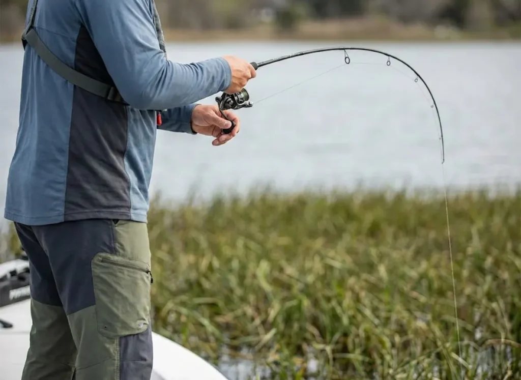 Side profile of a fisherman holding a fishing rod high with the line going vertically into a grass mat.