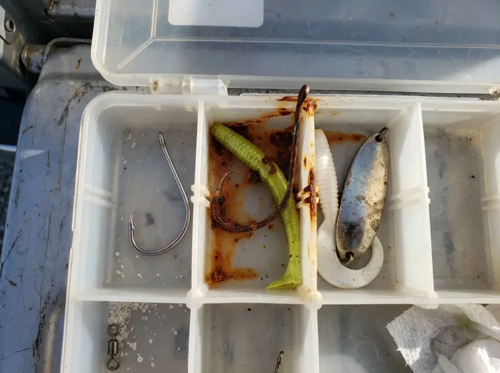A rusted hook bleeding rust across lures in a tackle tray, the terminal tackle risk in saltwater gear