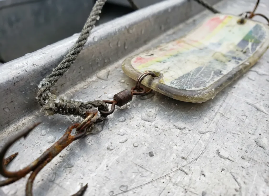 Close-up of a 360 flasher and fishing lure rigged with heavy line on a boat gunwale.