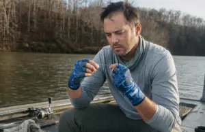 Best Fishing Gloves for Sun and Cold Water Days Angler in fingerless UPF fishing gloves retying a leader knot in low morning light on a boat