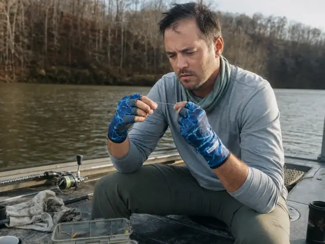 0-best-fishing-gloves-sun-cold-hero Angler in fingerless UPF fishing gloves retying a leader knot in low morning light on a boat