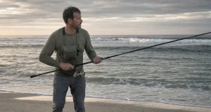 Best Surf Fishing Rods That Actually Reach Fish Angler on an open beach at dawn holding a surf fishing rod aimed at the trough