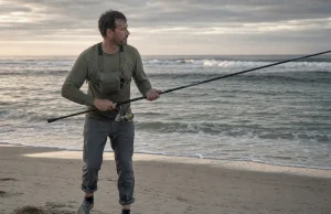 Best Surf Fishing Rods That Actually Reach Fish Angler on an open beach at dawn holding a surf fishing rod aimed at the trough