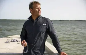 Does UPF Clothing Really Work? The Physics Says Yes Angler in a long sleeve UPF fishing shirt on open water at midmorning, sleeves down against full sun