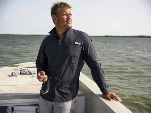 0-upf-clothing-physics-protection-hero Angler in a long sleeve UPF fishing shirt on open water at midmorning, sleeves down against full sun