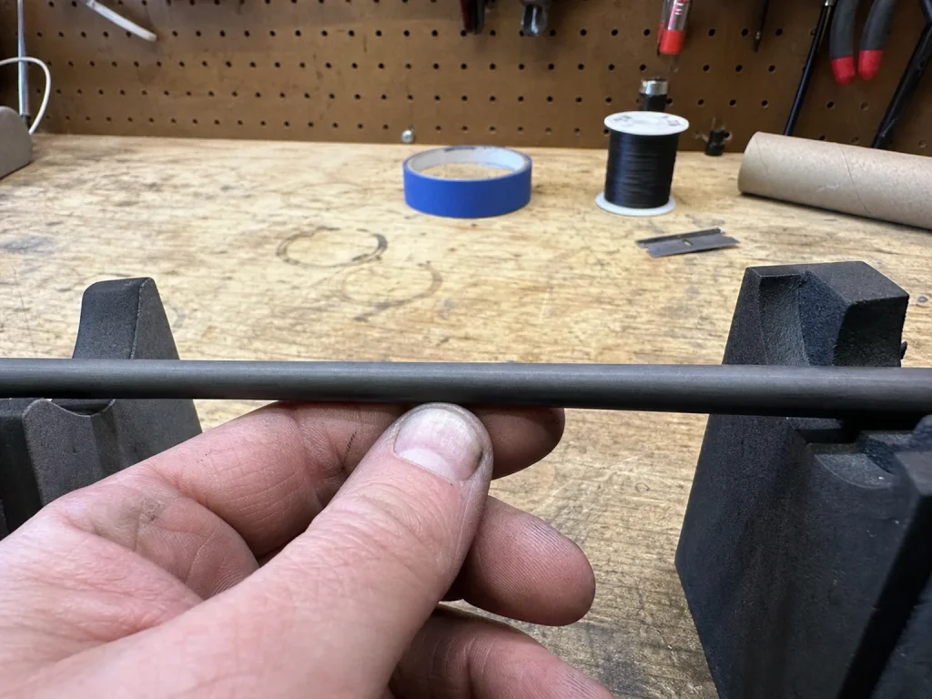 Close-up of a bare graphite rod blank on a rod-building bench showing the wall seam