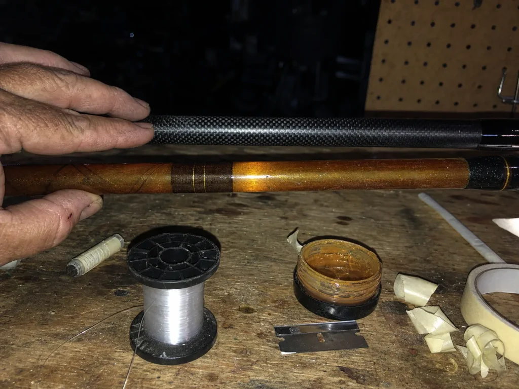 Close-up of a carbon fiber rod blank next to a fiberglass blank on a garage workbench under flash