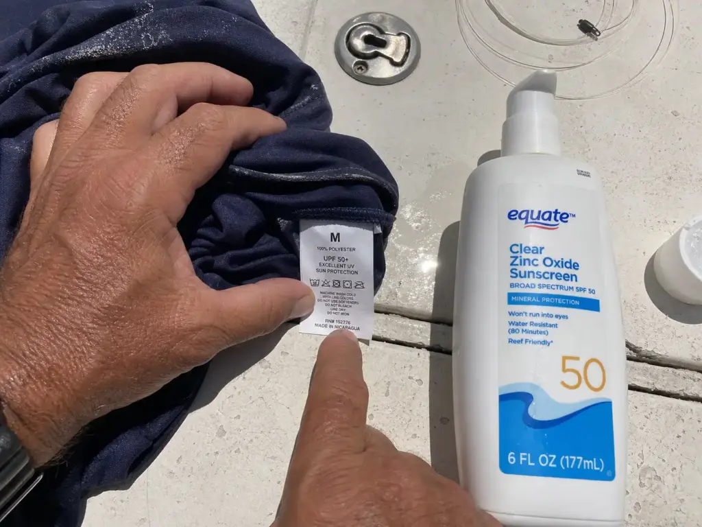 Hands holding a shirt tag showing a UPF rating next to a bottle of sunscreen on a boat deck