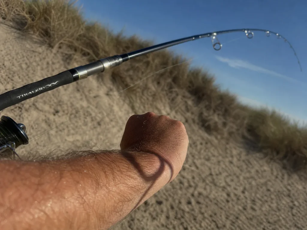 Angler flexing a surf rod under load to show its fast action bend