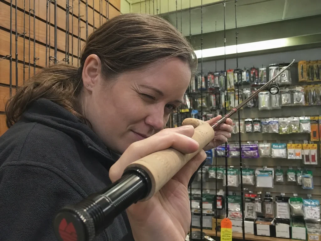 An angler sighting down a finished fishing rod blank at a tackle shop rack