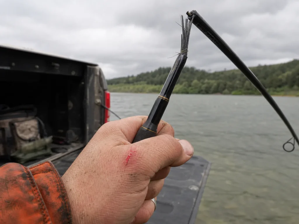 Close-up of a snapped graphite fishing rod blank showing splintered carbon fibers at the fracture