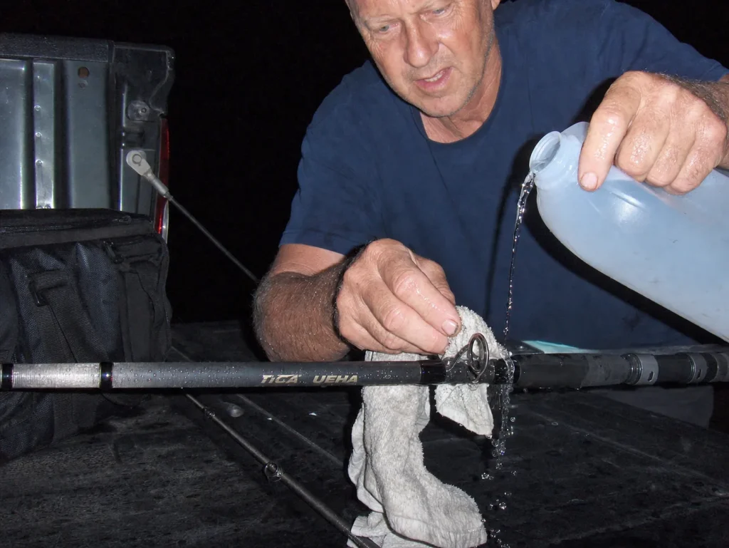 Angler rinsing a surf rod's guides with fresh water at the truck at dusk