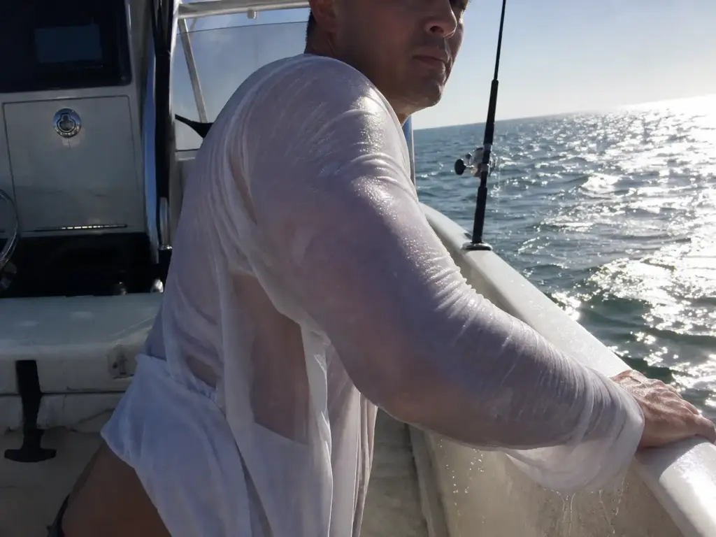 Soaked cotton shirt clinging to an angler's shoulder after a wave, fabric darkened and stretched thin