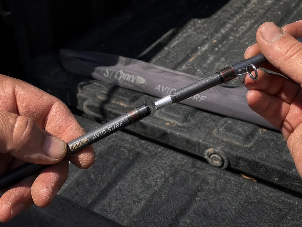 Angler separating a two-piece surf rod at the ferrule joint beside a truck