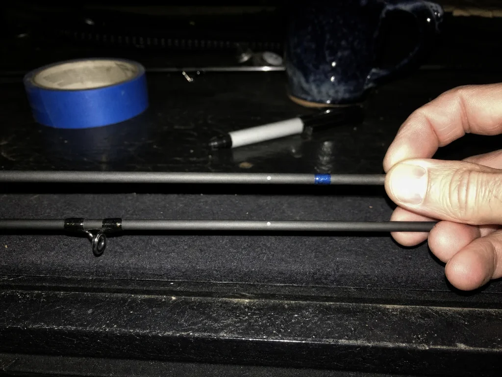Two sections of a multi-piece fishing rod laid on a bench with spine marks under flash