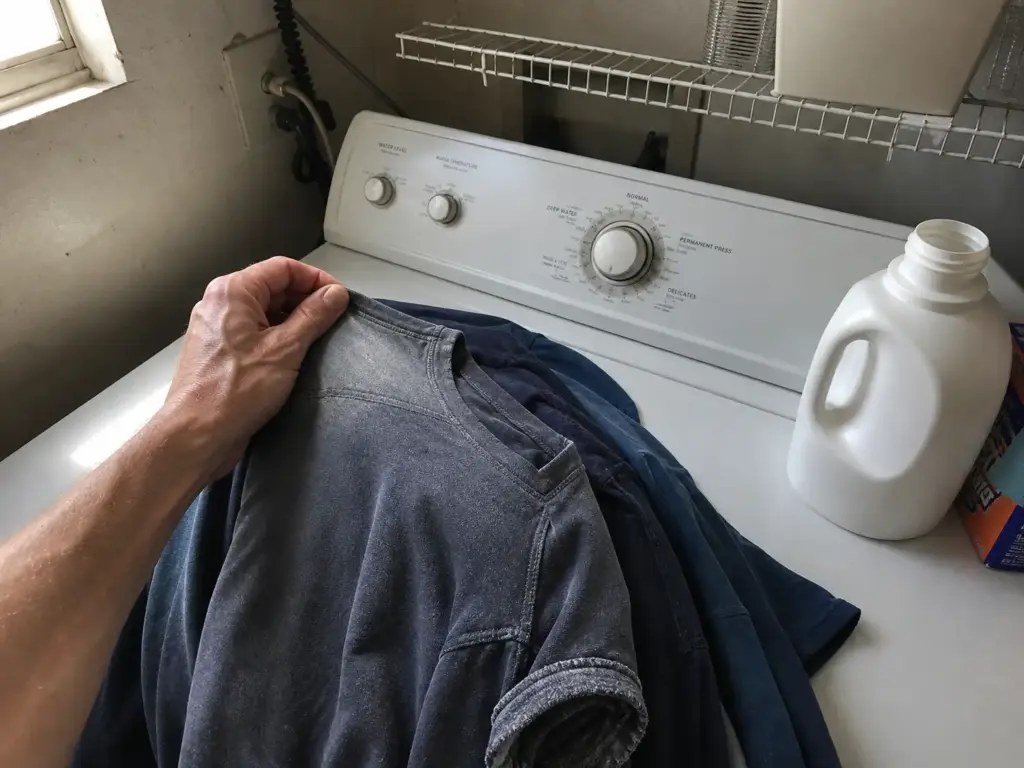 Faded UPF fishing shirts sorted on top of a washer, checked for wear before a cold wash cycle