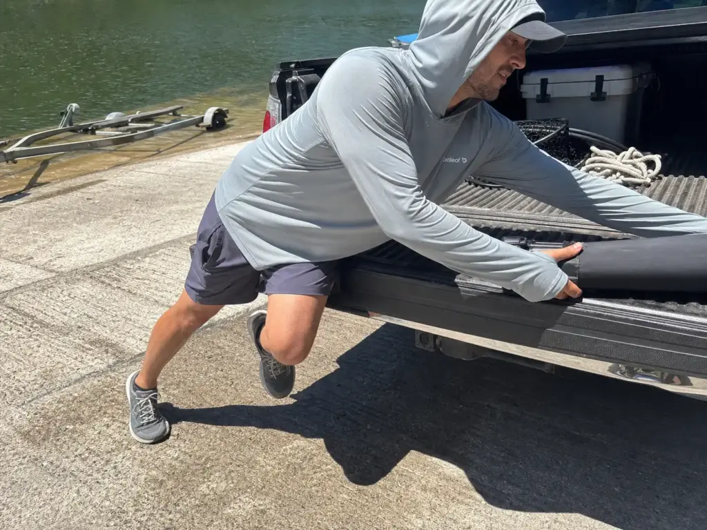 Angler in a budget UPF sun hoodie loading gear at the ramp, hood up against high sun