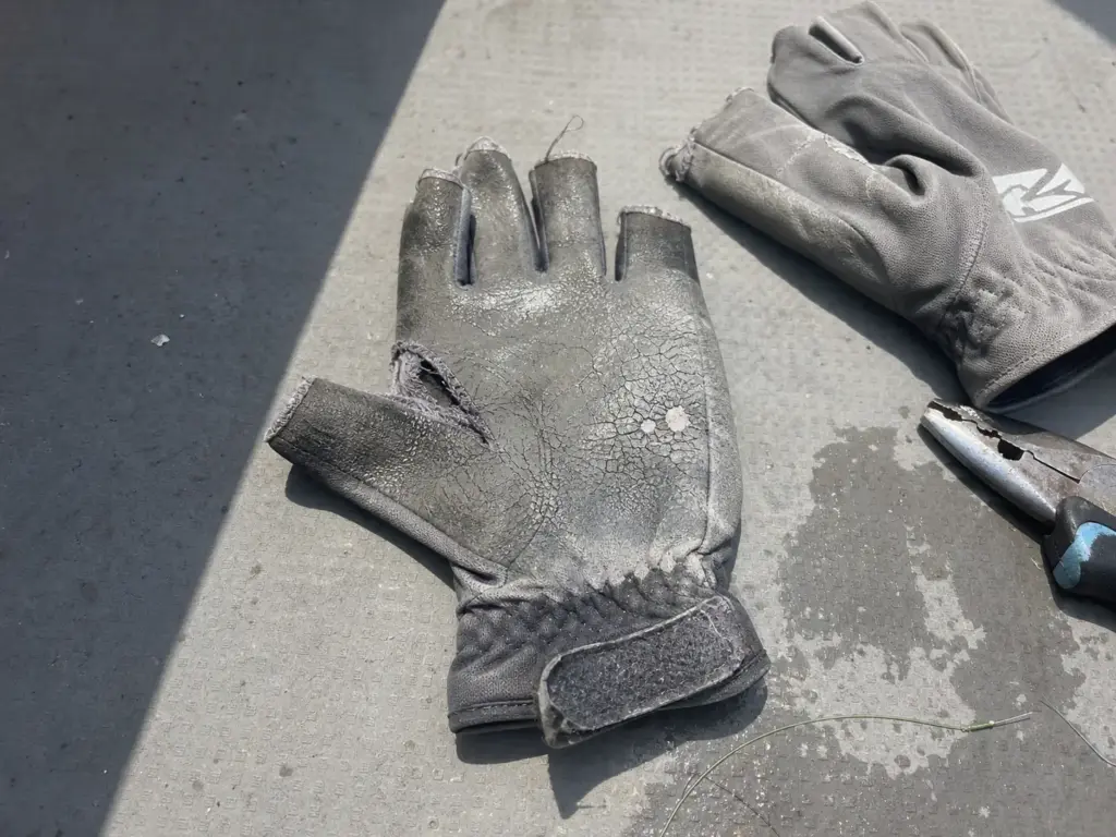 Worn out fishing glove with a split thumb seam and cracked palm coating lying on a boat deck