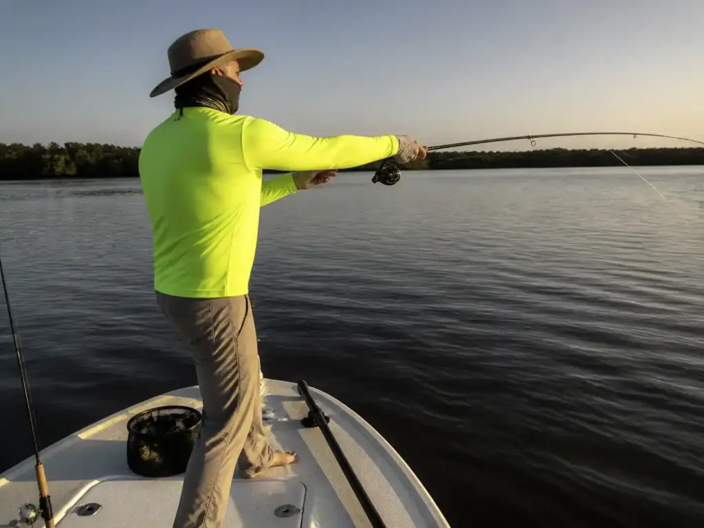 Angler covered head to hands in a UPF shirt, gaiter and wide brim hat during late day sun on the water