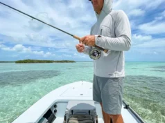 The Angler’s Blueprint to Saltwater Flats Ecosystems A professional angler standing on the bow of a skiff in crystal clear tropical waters, holding a fly rod, surrounded by a vast saltwater flats ecosystem.