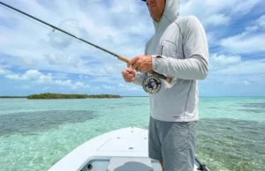 The Angler’s Blueprint to Saltwater Flats Ecosystems A professional angler standing on the bow of a skiff in crystal clear tropical waters, holding a fly rod, surrounded by a vast saltwater flats ecosystem.