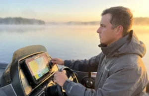Avoid Dead Zones: Fish Finder Transducer Cone Geometry Professional angler in a bass boat cockpit at dawn, looking focused, with a high-tech Lowrance fish finder screen glowing in the foreground.