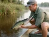 Best Digital Fish Scale Grip Without the Gimmicks Angler weighing a bass horizontally with a digital fish scale grip low over calm water