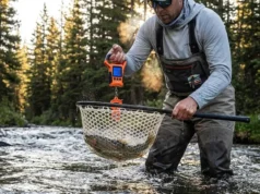 Best Digital Fish Scales: Grip & Weigh Angler standing in a river at sunrise weighing a trout inside a landing net using a digital scale.