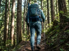 Best Fishing Backpacks: Hiking & Bank Anglers Angler hiking up a steep forest trail wearing a fully loaded fishing backpack with rod tube attached.