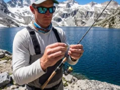 Best Swimbait Jigheads: Weedless vs Exposed Angler inspecting a swimbait jighead on a granite shoreline at a high-altitude mountain lake.