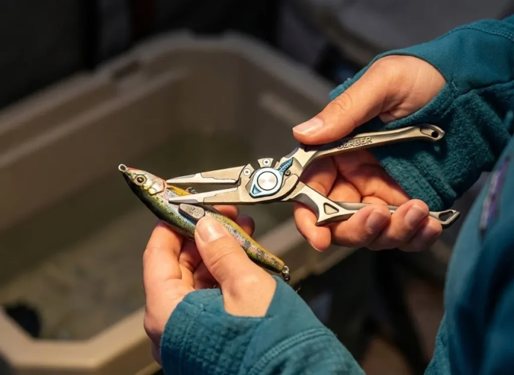 Close-up of angler's hands using pliers to apply weight to a fishing lure for buoyancy testing.