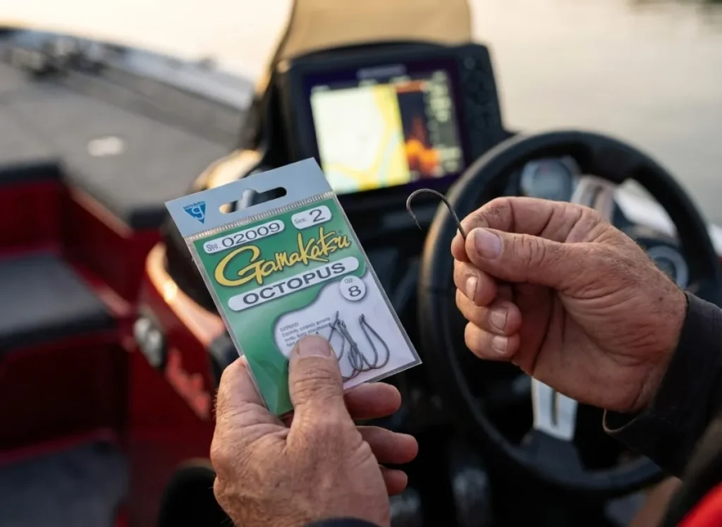 Angler comparing a new pack of Gamakatsu hooks to a used dull hook on a boat console.