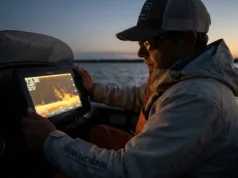 CHIRP Sonar Frequencies Explained: Depth & Species Angler looking at Garmin GPSMAP sonar screen in low light wearing Grundens gear.